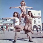 Barney Frye lifts three women (Joan Greenman, Sherry Lee Evans, Kim Curtis) on the boardwalk, Muscle Beach, 1956